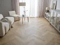 Jasna podłoga w jodełkę w salonie, z beżową kanapą i fotelami, tworzy przytulną atmosferę.