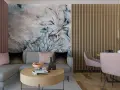 Elegancki salon z sofą i stolikiem kawowym w odcieniach brązu i pudrowego różu. Na ścianie duża, malarska tapeta z kwiatowym motywem.