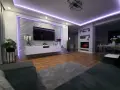 Nowoczesne oświetlenie ściany za telewizorem w salonie, podkreślające ceglaną fakturę i tworzące nastrojową atmosferę.