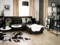 Nowoczesny salon z czarną ścianą w tle, czarną sofą, białymi stolikami i dywanem w cętki.