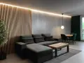 Nowoczesny salon w stylu loft. Aranżacje z szarą sofą, drewnianą ścianką i zielonymi akcentami.