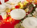 Elegancko nakryty stół na Wigilię: biała zastawa, złote ozdoby, choinkowe lampki i świece tworzą magiczny nastrój.