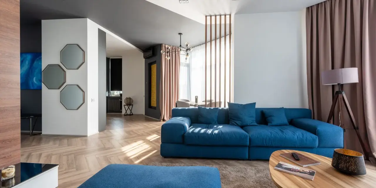 Granatowa sofa z niebieskimi poduszkami, stolik kawowy, dywan i lampa tworzą przytulną przestrzeń.