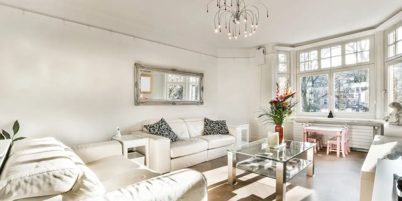 Jasny salon z białymi sofami, szklanym stolikiem i ozdobnym lustrem. Inspiracje salonem w stylu francuskim.