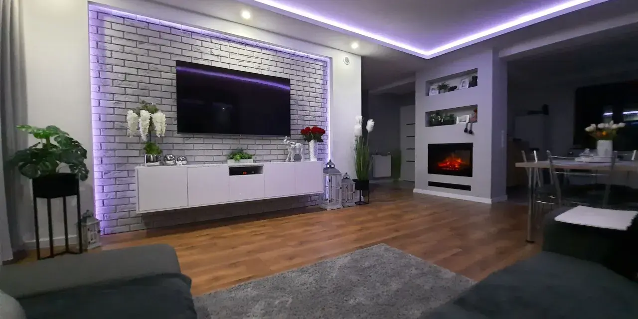 Nowoczesne oświetlenie ściany za telewizorem w salonie, podkreślające ceglaną fakturę i tworzące nastrojową atmosferę.