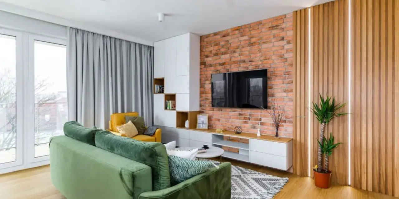 Nowoczesny salon z zieloną kanapą, żółtym fotelem, ceglaną ścianą i pionowymi lamelami.