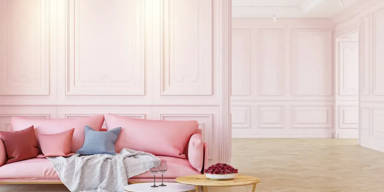 Elegancka różowa kanapa i stoliki kawowe na tle subtelnej sztukaterii ściennej. Inspiracje dla Twojego wnętrza.