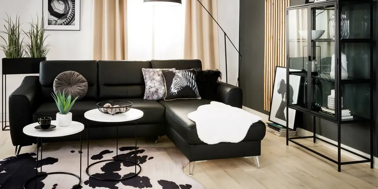 Nowoczesny salon z czarną ścianą w tle, czarną sofą, białymi stolikami i dywanem w cętki.