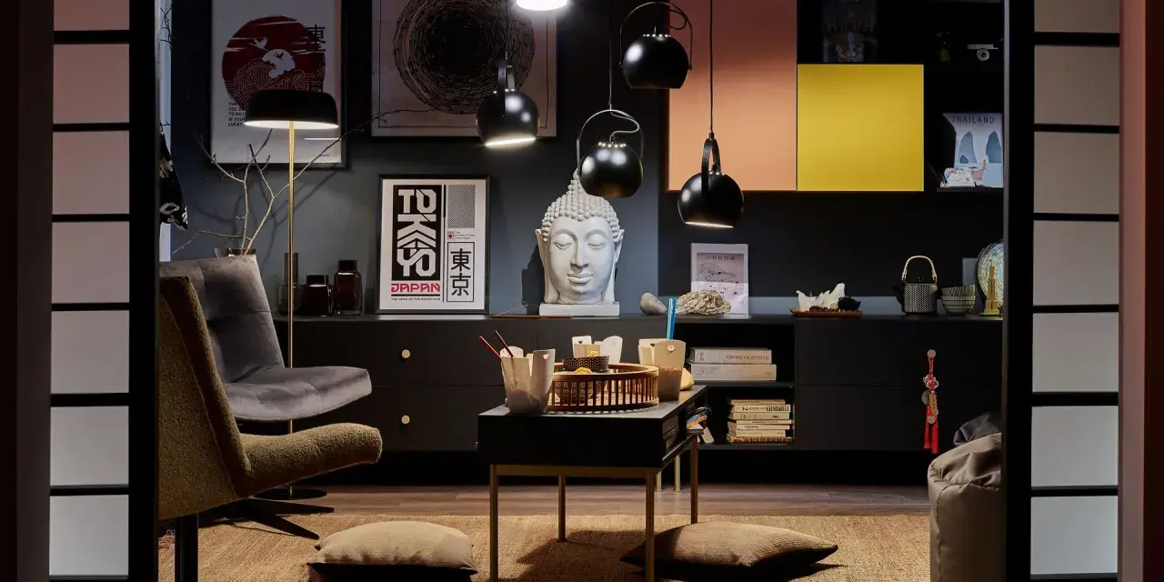Salon w stylu eklektycznym z motywami azjatyckimi. Wygodne fotele, stolik z poduszkami, rzeźba Buddy i plakaty z Japonii tworzą przytulną atmosferę.