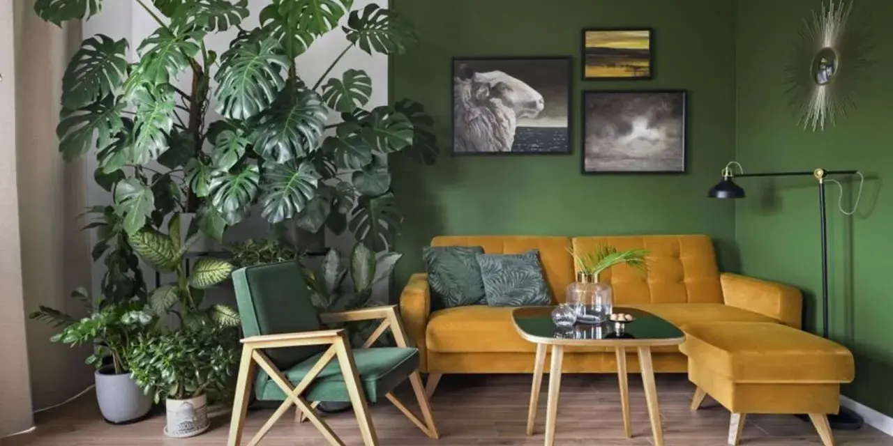 Zielony kącik z kwiatami w salonie. Monstera i inne rośliny tworzą bujną dżunglę obok musztardowej kanapy i fotela.