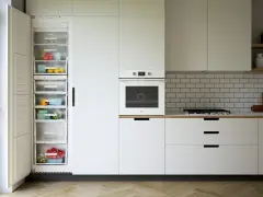 Nowoczesna kuchnia z otwartą lodówką pełną świeżych warzyw i owoców, piekarnikiem i szufladami co pod szafki kuchenne.