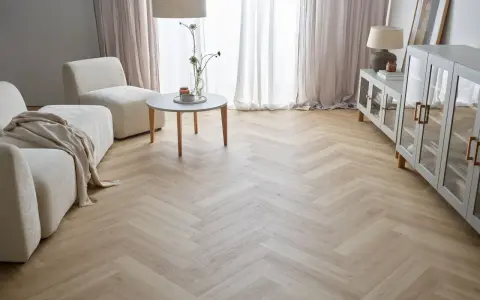 Jasna podłoga w jodełkę w salonie, z beżową kanapą i fotelami, tworzy przytulną atmosferę.