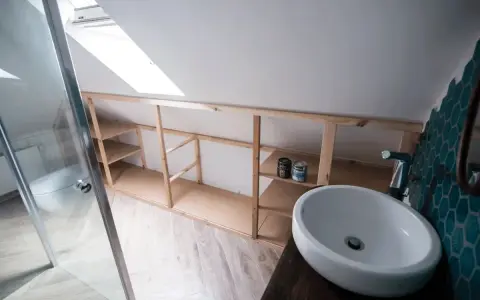 Drewniana konstrukcja łazienkowa, która pomoże Ci dowiedzieć się, jak zrobić szafkę pod umywalkę. Widać umywalkę, prysznic i farby.