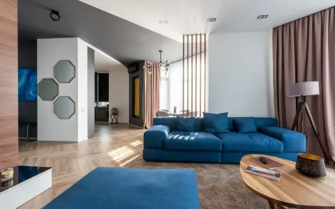 Granatowa sofa z niebieskimi poduszkami, stolik kawowy, dywan i lampa tworzą przytulną przestrzeń.