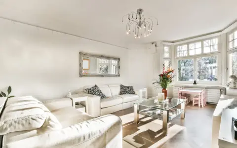 Jasny salon z białymi sofami, szklanym stolikiem i ozdobnym lustrem. Inspiracje salonem w stylu francuskim.