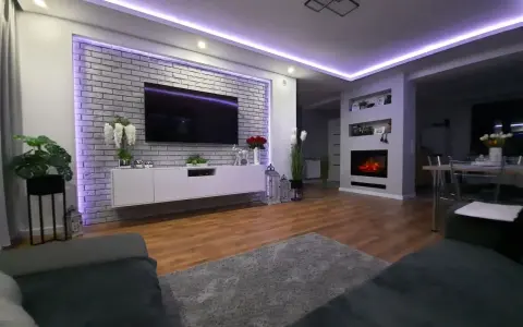 Nowoczesne oświetlenie ściany za telewizorem w salonie, podkreślające ceglaną fakturę i tworzące nastrojową atmosferę.