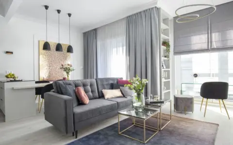 Elegancka dekoracja okien w salonie z szarymi zasłonami i białym woalem. Miękki dywan i stylowe meble tworzą przytulną atmosferę.