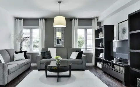 Nowoczesny salon z ciemnymi meblami, szarymi sofami i czarnym stolikiem kawowym. Aranżacje podkreślają elegancję i minimalizm.