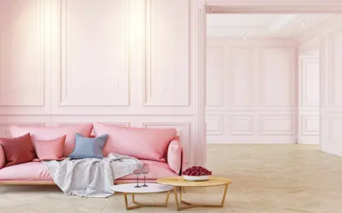 Elegancka różowa kanapa i stoliki kawowe na tle subtelnej sztukaterii ściennej. Inspiracje dla Twojego wnętrza.
