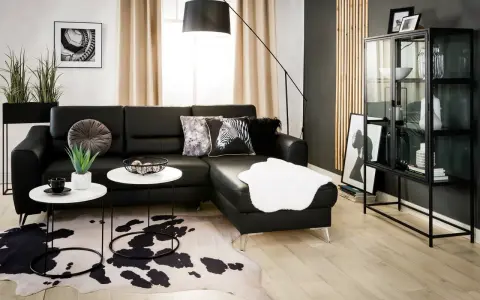 Nowoczesny salon z czarną ścianą w tle, czarną sofą, białymi stolikami i dywanem w cętki.