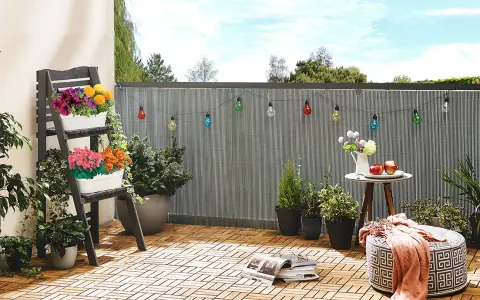 Kolorowe lampki i kwiaty tworzą przytulny balkon tanim kosztem. Drewniana podłoga i wygodne siedzisko zapraszają do relaksu.