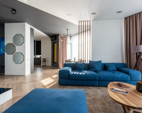 Granatowa sofa z niebieskimi poduszkami, stolik kawowy, dywan i lampa tworzą przytulną przestrzeń.