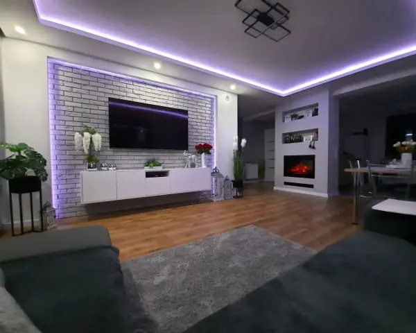 Nowoczesne oświetlenie ściany za telewizorem w salonie, podkreślające ceglaną fakturę i tworzące nastrojową atmosferę.