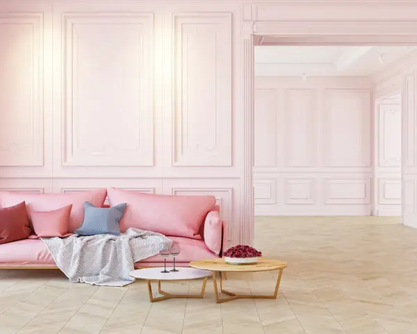Elegancka różowa kanapa i stoliki kawowe na tle subtelnej sztukaterii ściennej. Inspiracje dla Twojego wnętrza.