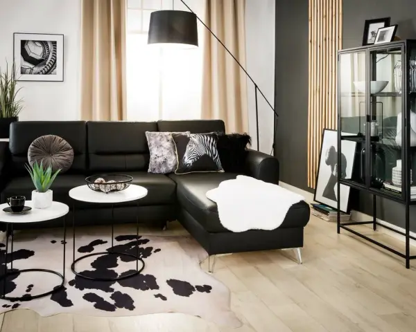 Nowoczesny salon z czarną ścianą w tle, czarną sofą, białymi stolikami i dywanem w cętki.