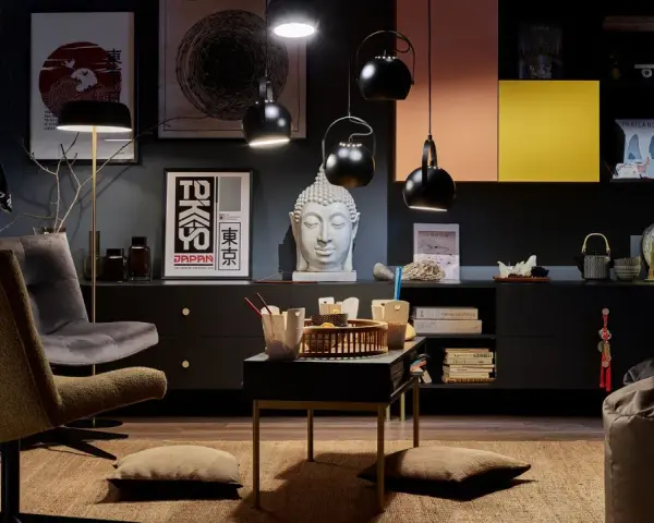 Salon w stylu eklektycznym z motywami azjatyckimi. Wygodne fotele, stolik z poduszkami, rzeźba Buddy i plakaty z Japonii tworzą przytulną atmosferę.