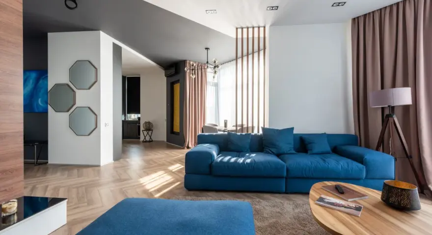 Granatowa sofa z niebieskimi poduszkami, stolik kawowy, dywan i lampa tworzą przytulną przestrzeń.
