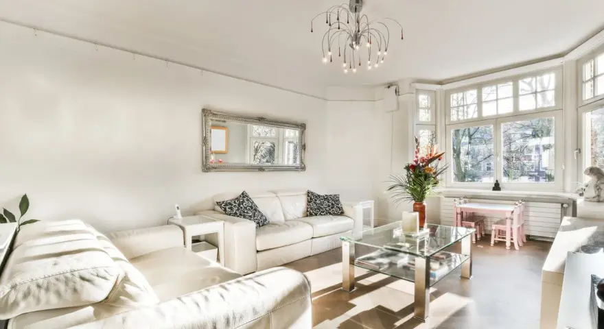Jasny salon z białymi sofami, szklanym stolikiem i ozdobnym lustrem. Inspiracje salonem w stylu francuskim.