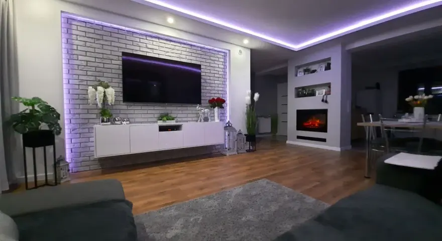 Nowoczesne oświetlenie ściany za telewizorem w salonie, podkreślające ceglaną fakturę i tworzące nastrojową atmosferę.