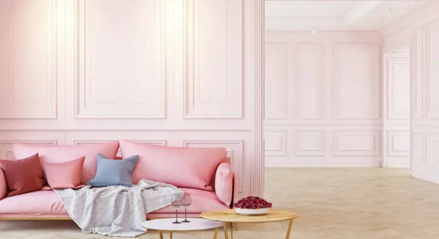 Elegancka różowa kanapa i stoliki kawowe na tle subtelnej sztukaterii ściennej. Inspiracje dla Twojego wnętrza.