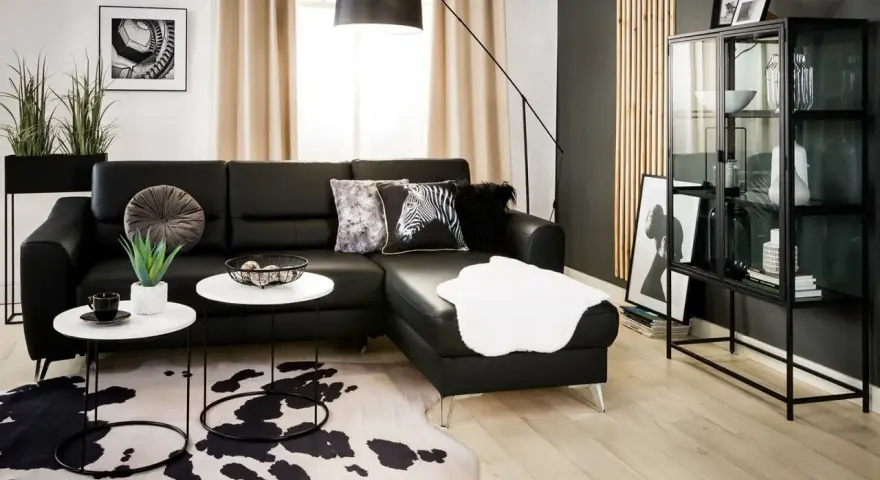 Nowoczesny salon z czarną ścianą w tle, czarną sofą, białymi stolikami i dywanem w cętki.