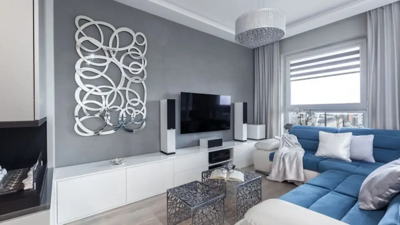 Nowoczesny biało szary salon aranżacje z niebieską kanapą, lustrzaną dekoracją ścienną i minimalistycznym umeblowaniem.