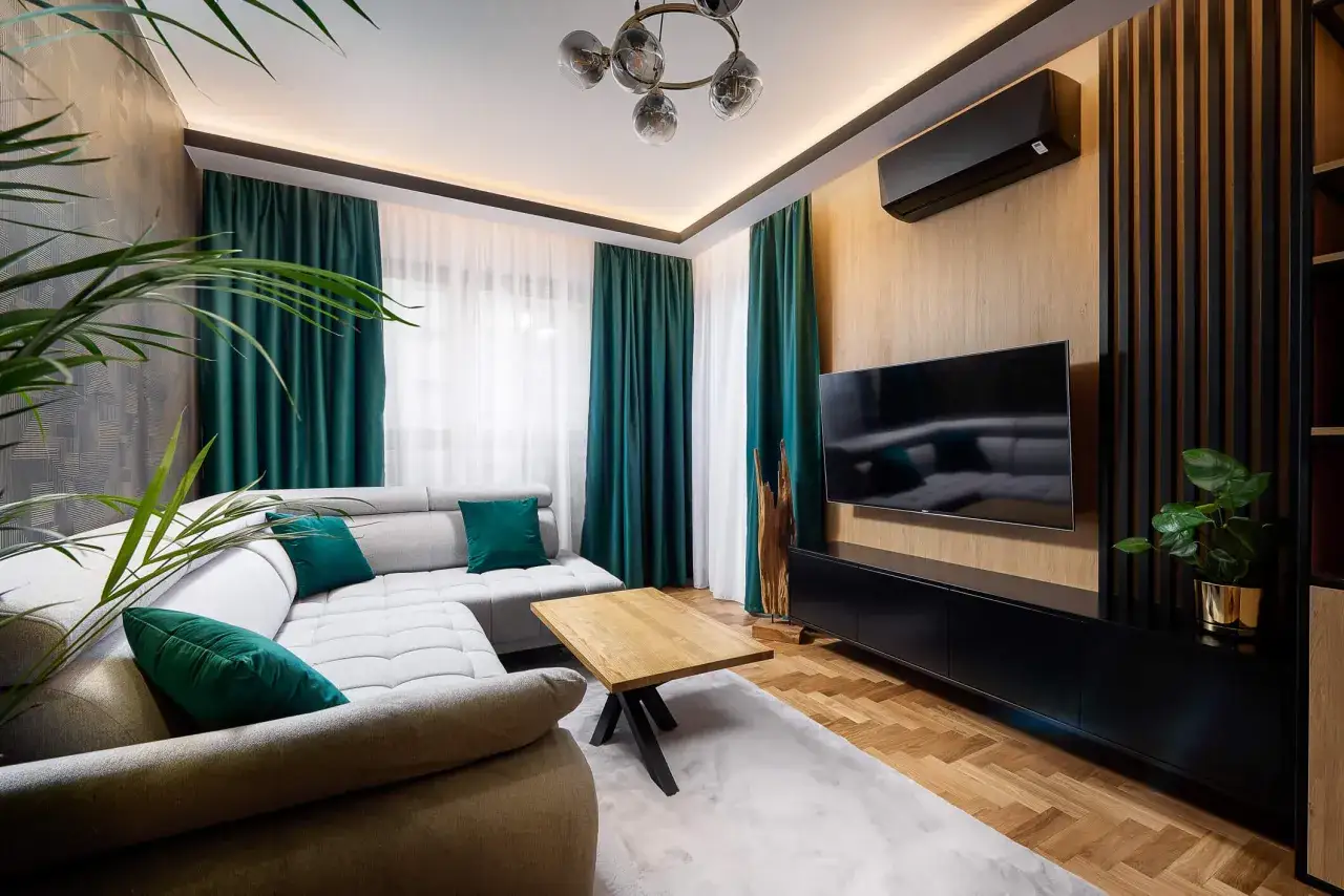 Nowoczesny salon w stylu eklektycznym. Szara kanapa z zielonymi poduszkami, drewniany stolik i zasłony tworzą przytulną atmosferę.