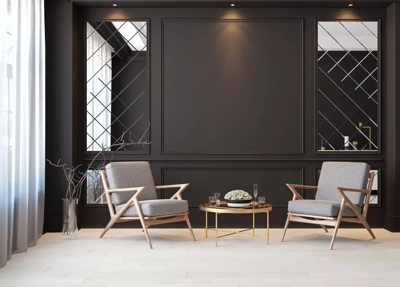 Elegancki salon z dwoma szarymi fotelami i złotym stolikiem. Centralnym punktem jest czarna ściana w salonie z ozdobnymi panelami i lustrami.
