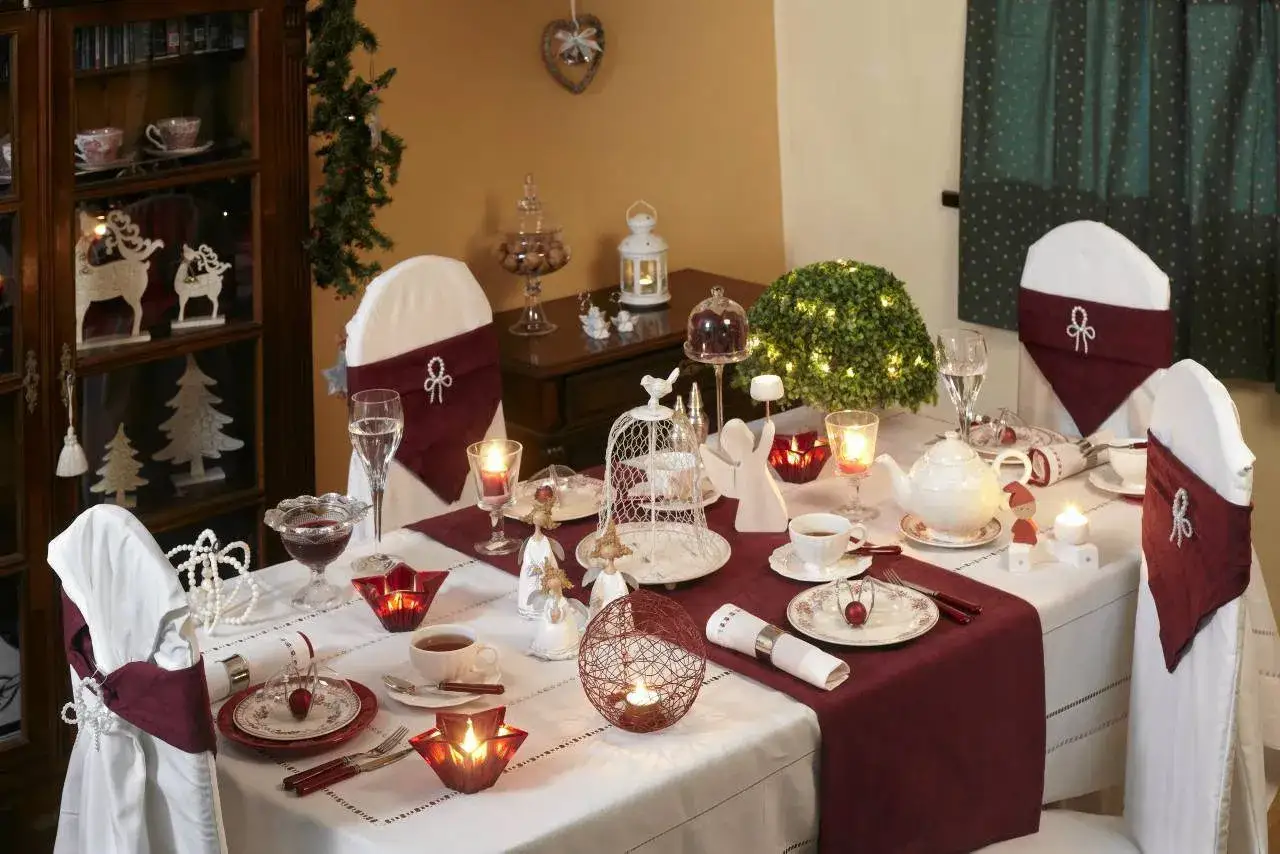 Elegancko nakryty stół na Wigilię: białe obrusy, bordowe bieżniki, świece, porcelana i świąteczne dekoracje.
