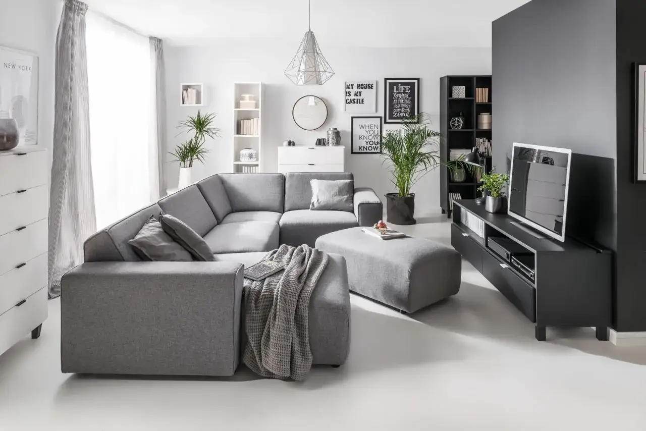 Szary salon z wygodną kanapą i pufą, inspiracja, jak ocieplić szary salon. Dodatki i rośliny dodają przytulności.